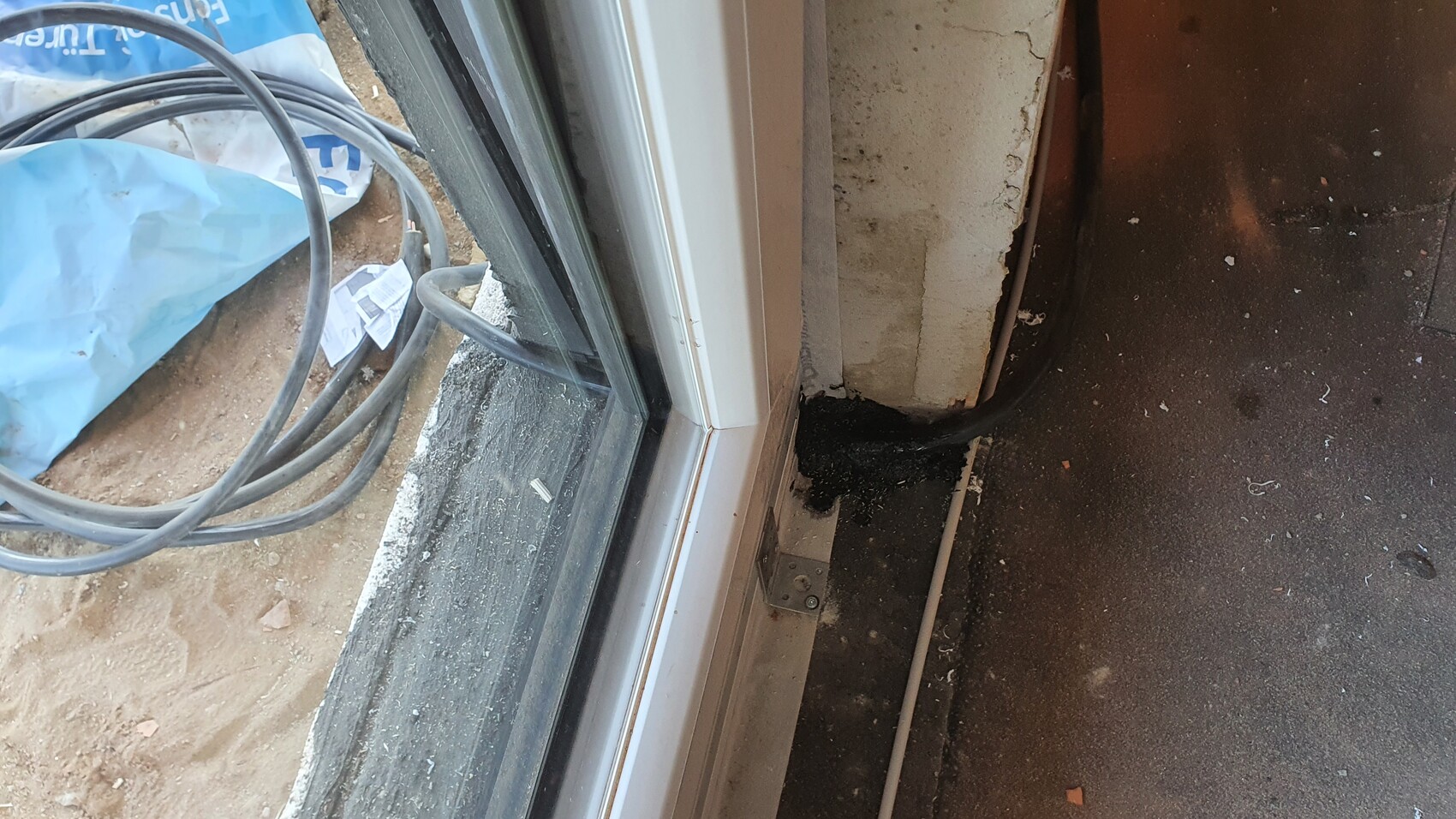 Door threshold with black sealant around conduit; cable reels and construction waste outside.