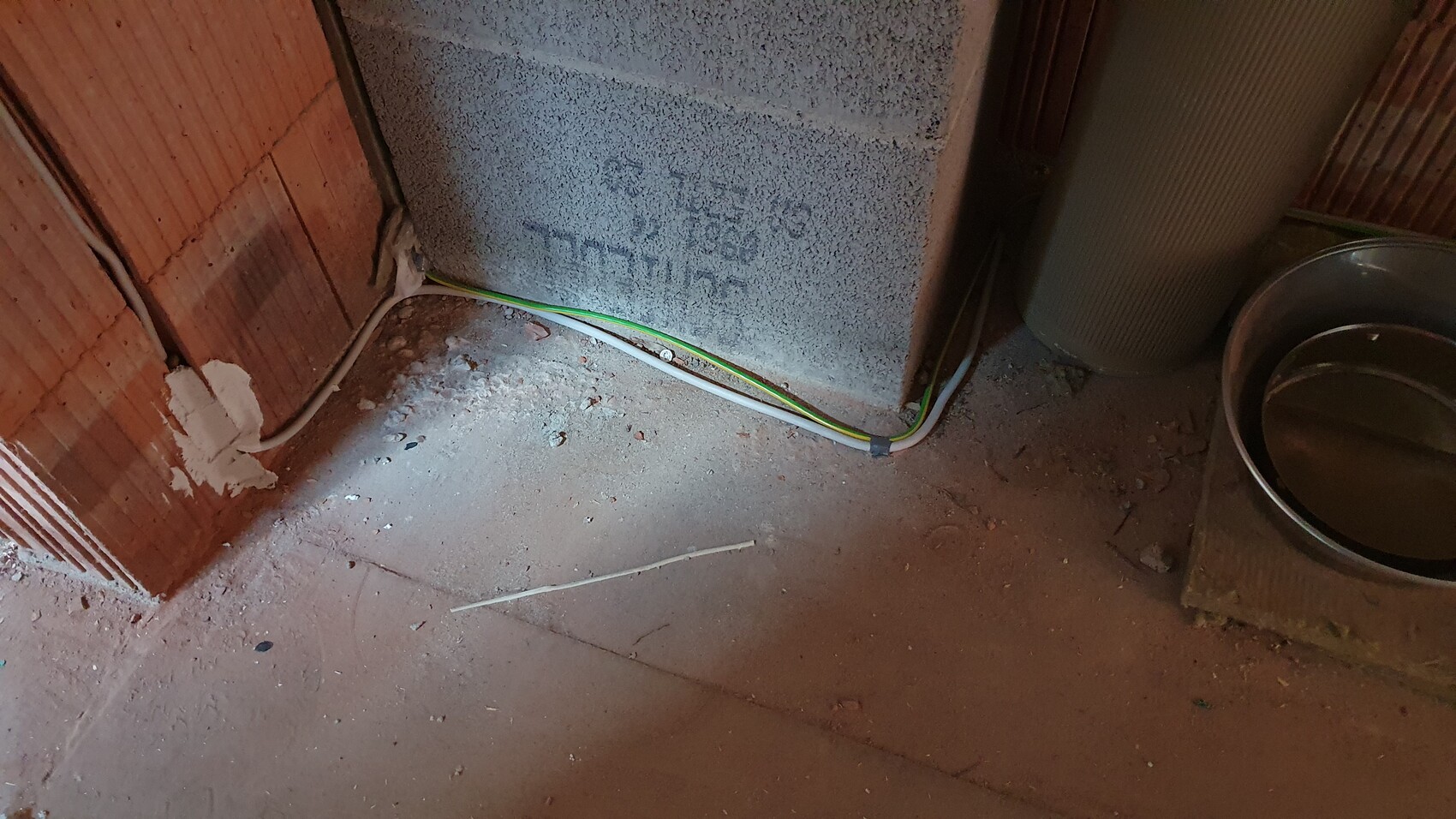 Basement room: exposed green-yellow and white cables on dusty floor near a brick wall.