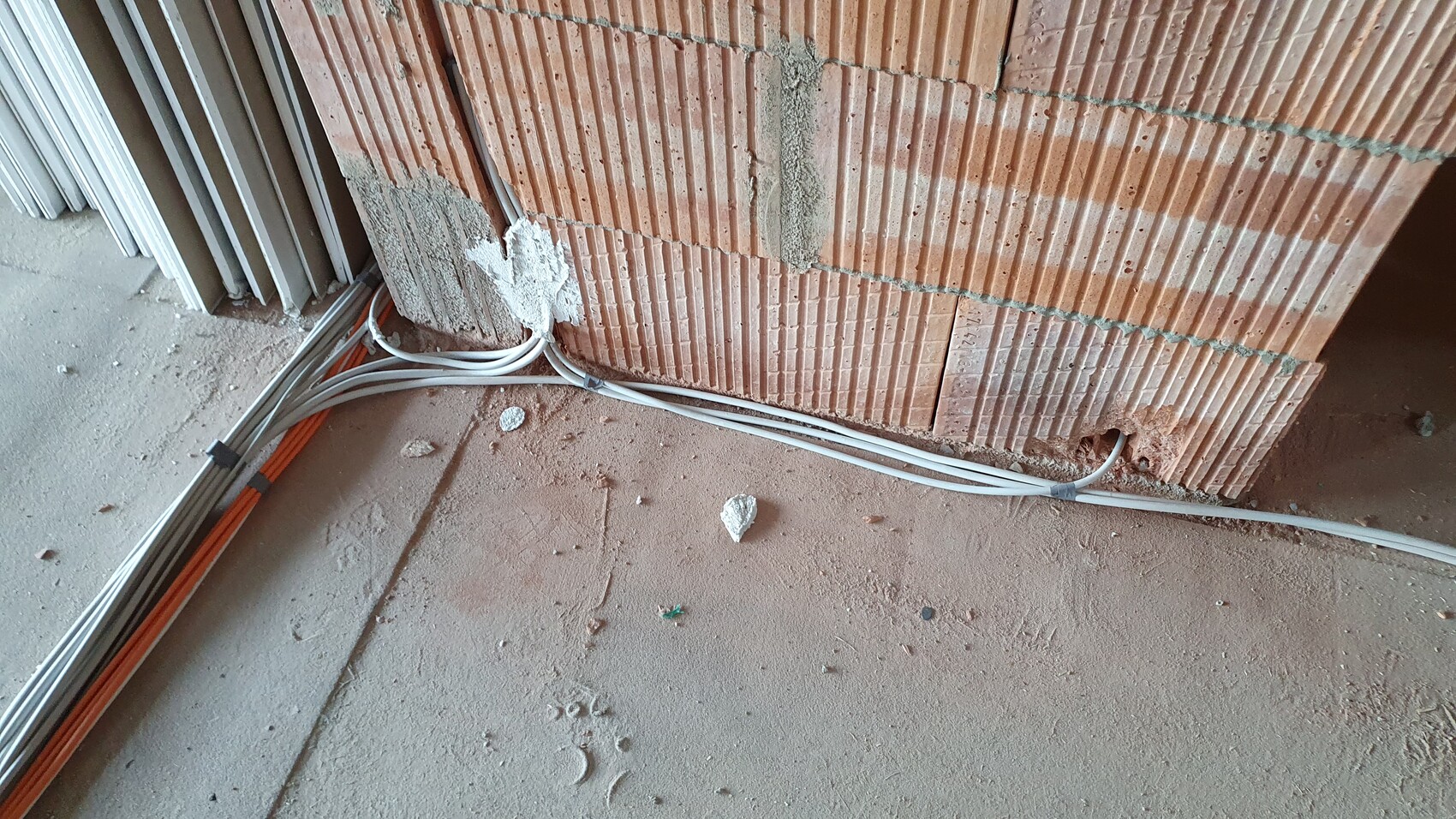 Construction site: unplastered brick wall, white and orange cables laid along the floor.