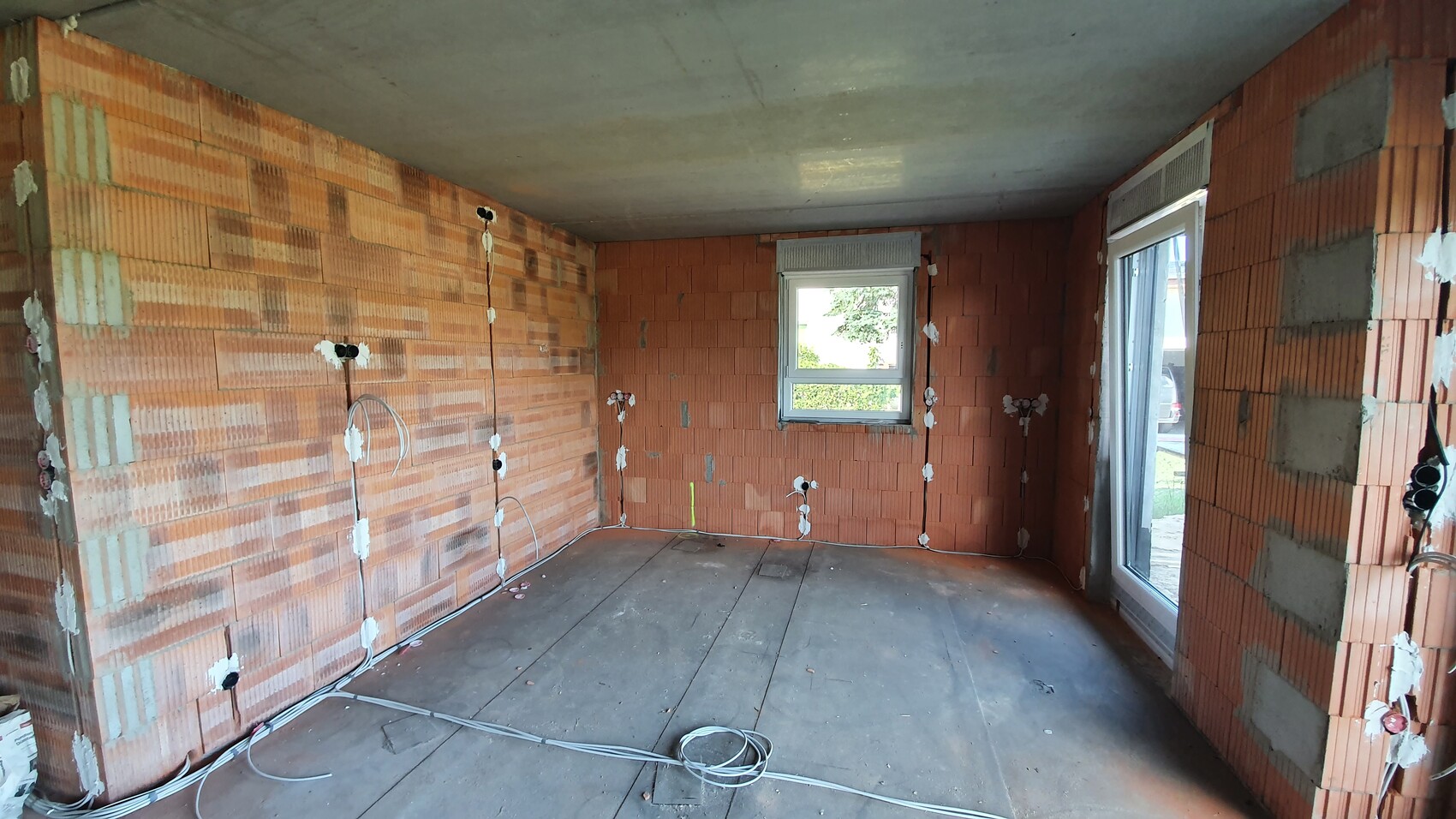 Unplastered interior: orange brick walls, visible electrical work, and window to the outside.
