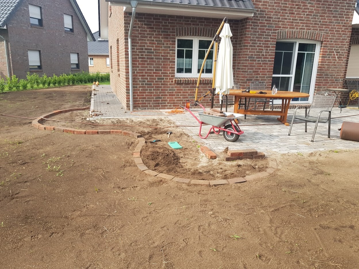 Garden construction site in front of the house with a round rubble stone bed edging, wheelbarrow, table and chairs.