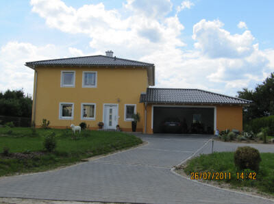 Exterior view of a yellow single-family house with carport, driveway, and garden