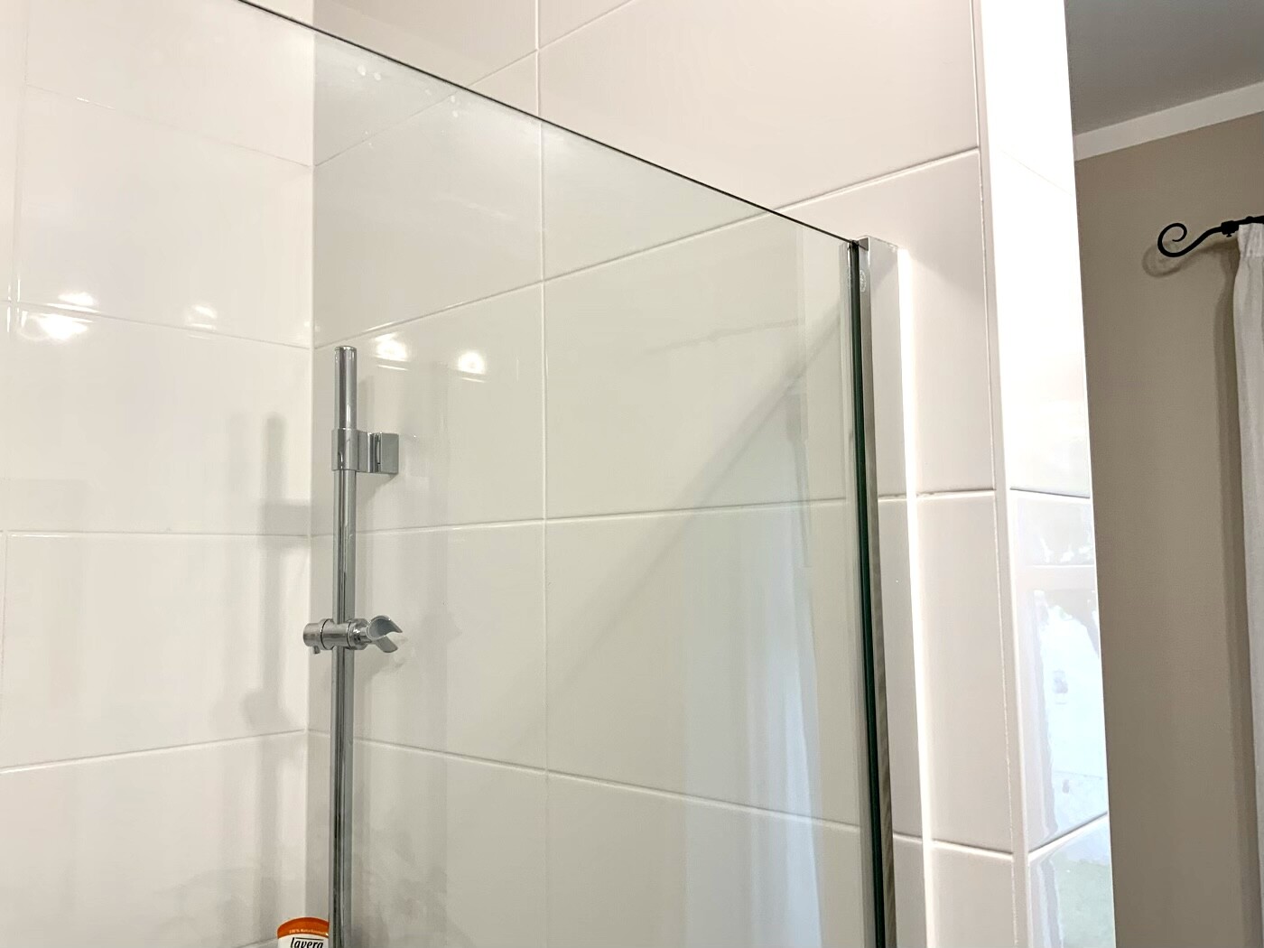 Shower enclosure with glass panel, metal guide, white tiles; orange container in the bottom left.