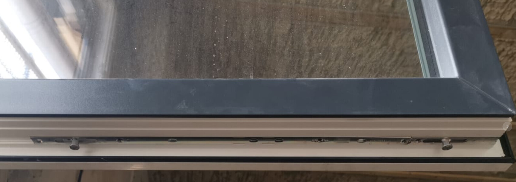 Close-up of a metal window frame with locking knobs and glass; view outside.