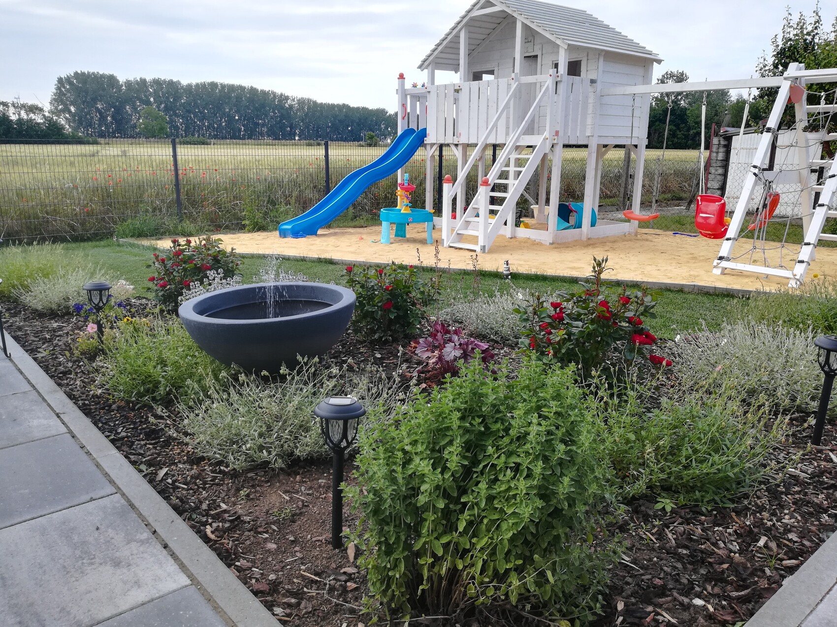 Garten mit weißem Holz-Spielturm, blauer Rutsche, Sandkasten und Schaukel.