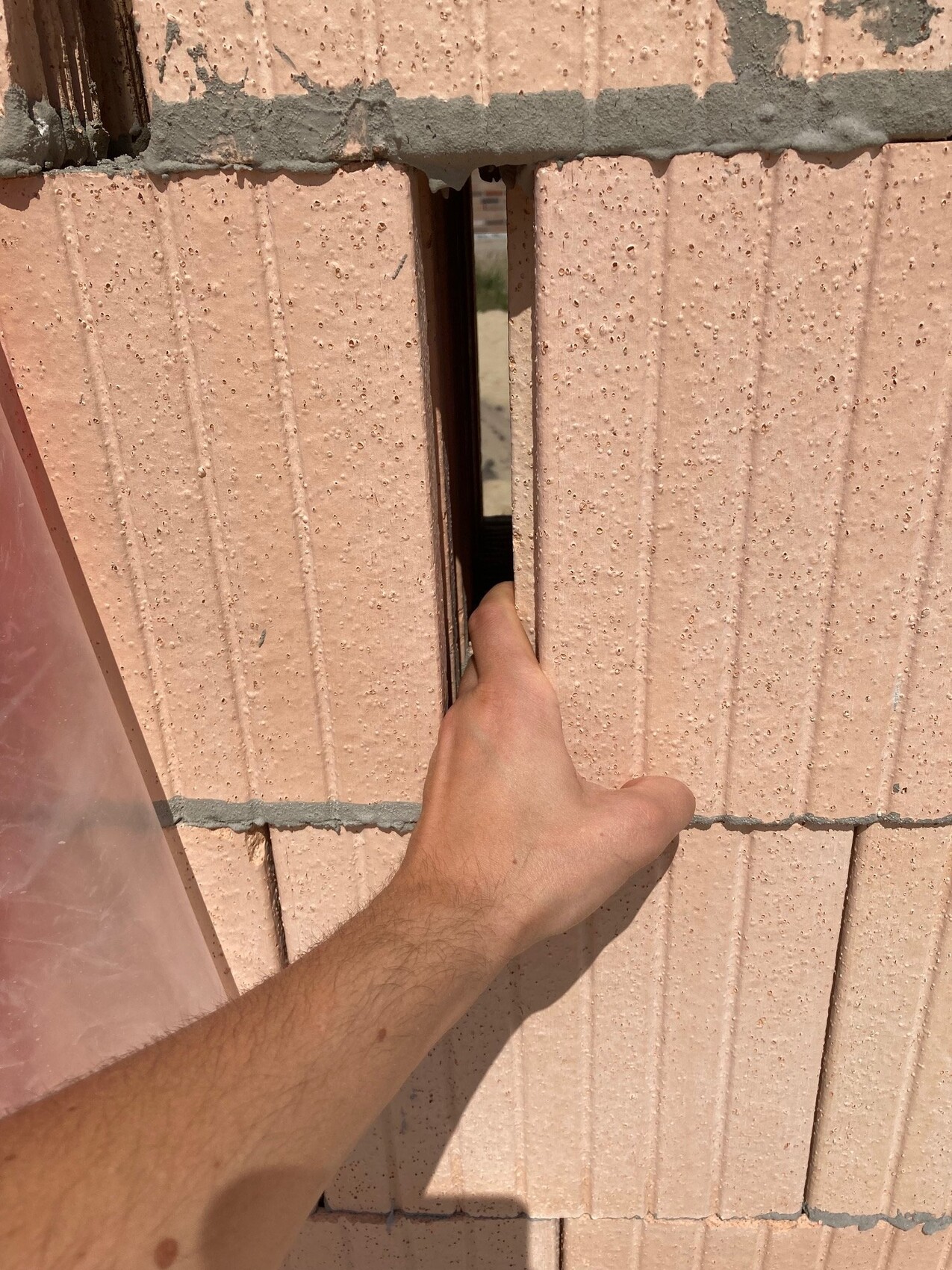 Hand inserting finger through narrow gap between pink concrete blocks, view into darkness behind.