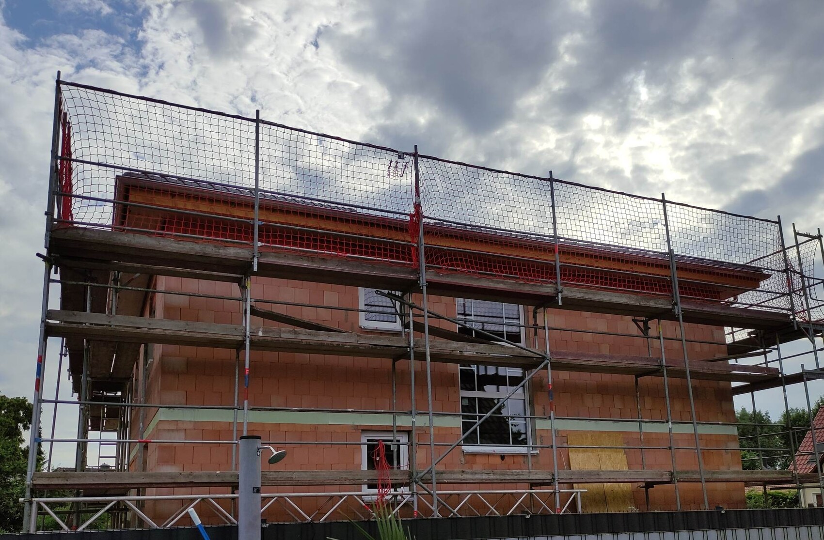 Baugerüst um ein rotes Backstein-Haus unter Bauarbeiten; bewölkter Himmel im Hintergrund.