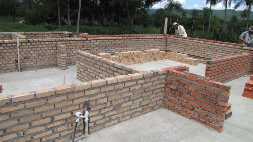 Construction site with brick walls and structural foundation, interior spaces under construction.
