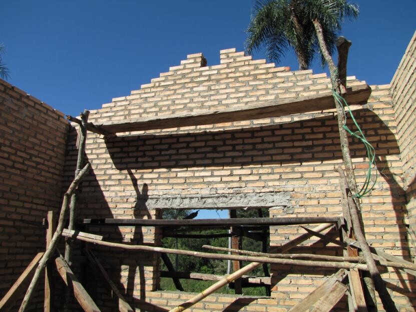 Construction site with brick wall, scaffolding, and wooden beams against blue sky.