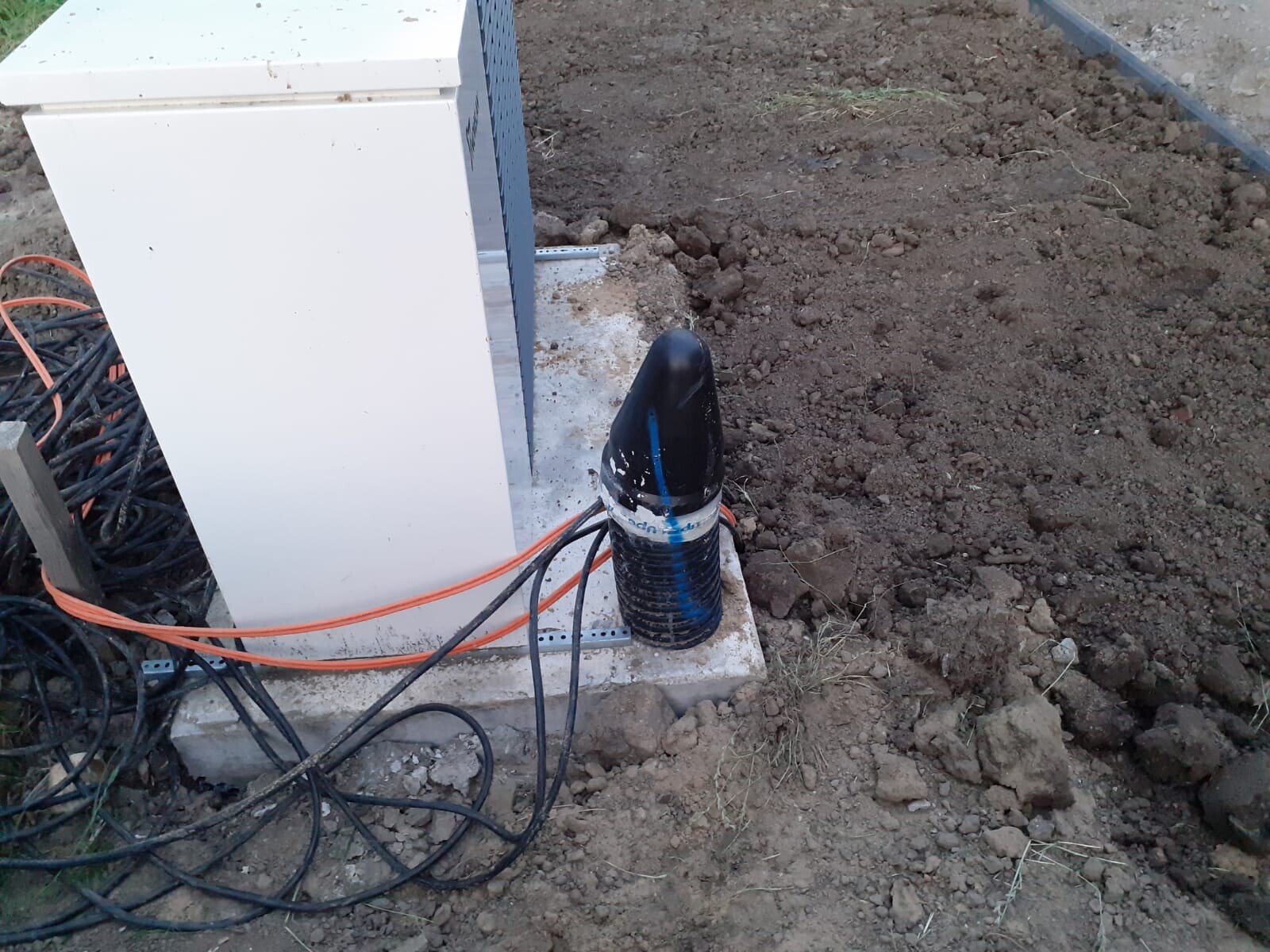 Outdoor air conditioning unit on concrete foundation, cable mess of black and orange cables in the ground.