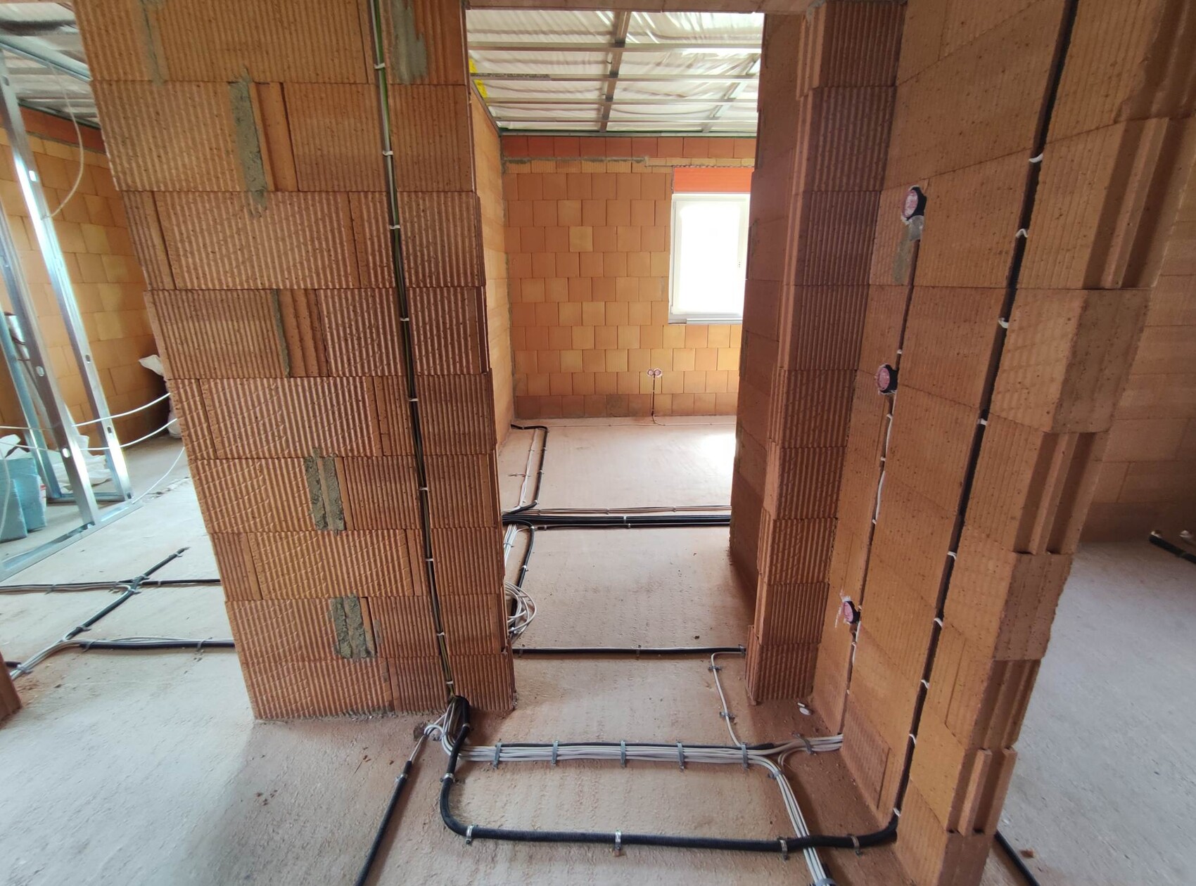 Shell construction room with brick walls, visible cable ducts on the floor, window in the background.