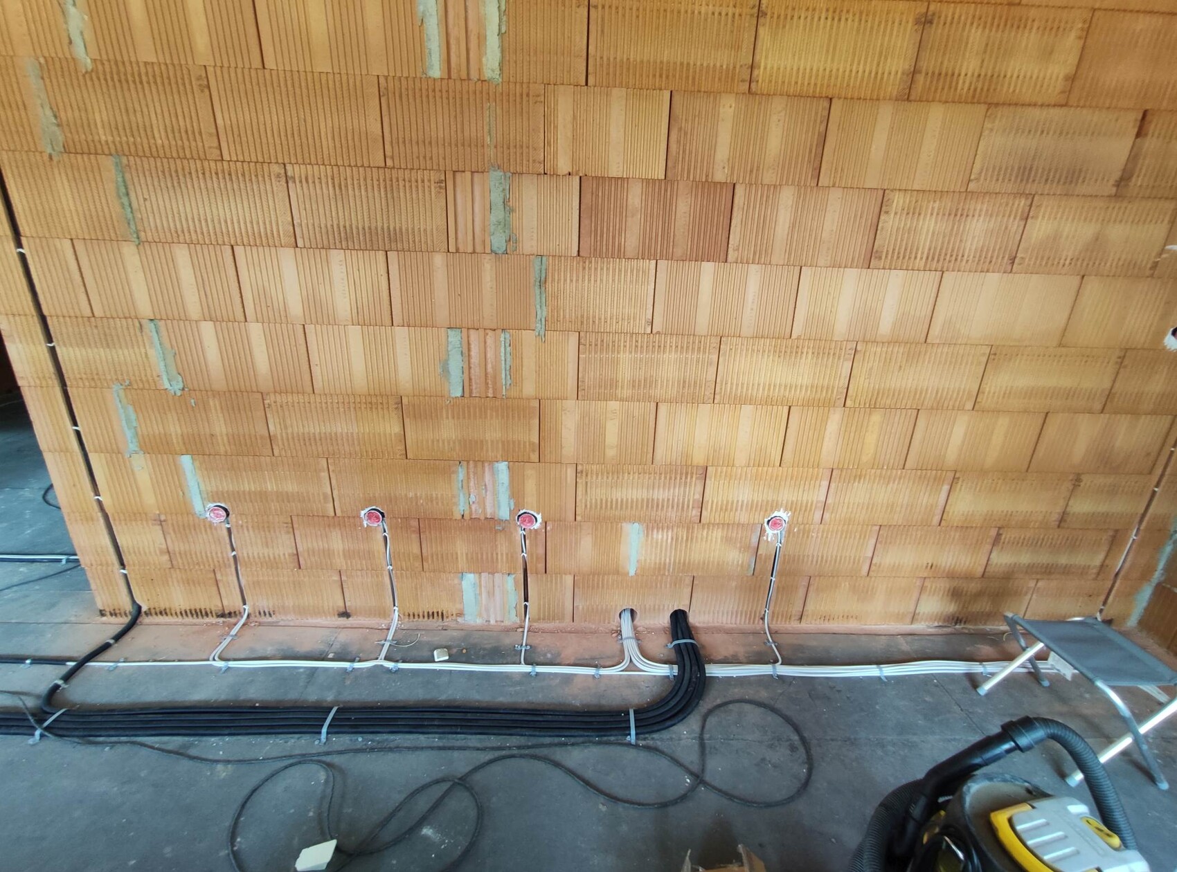 Construction site: brick wall with cable ducts, cables and sockets on the floor.