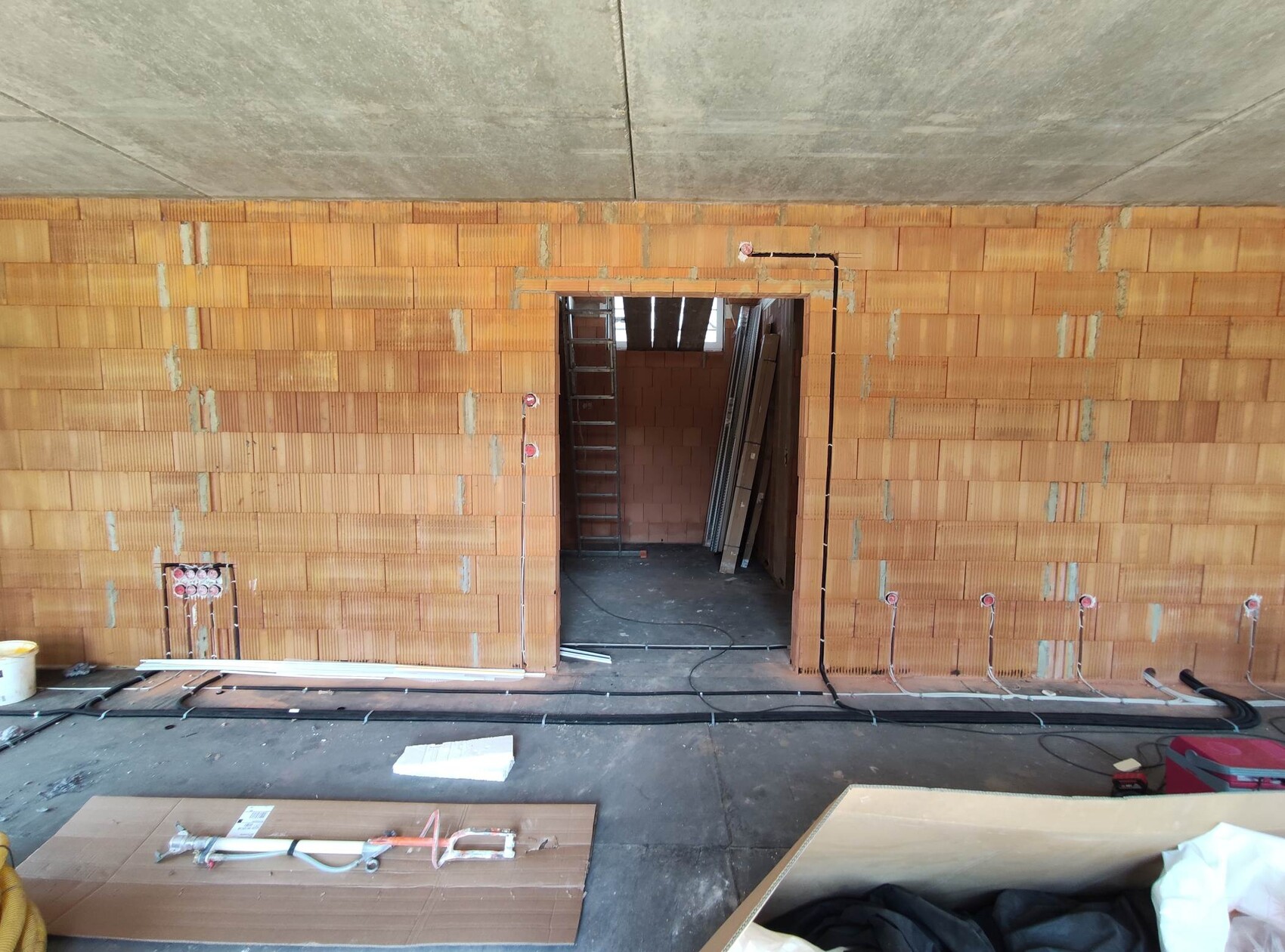 Construction site: unfinished brick wall, open passage, ladder, cables and building materials on the floor.
