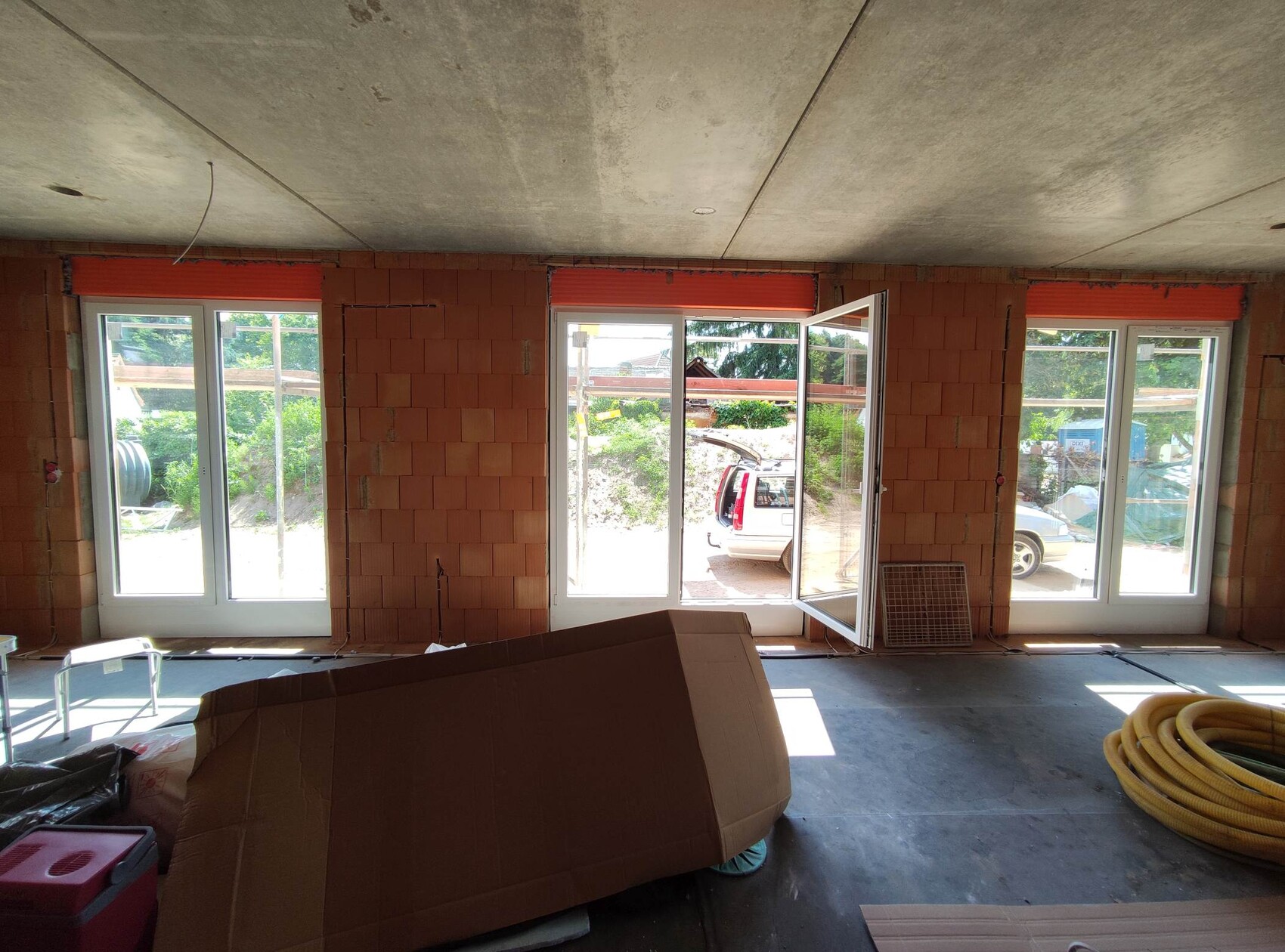 Unfinished interior of a house under construction; red brick walls, glass sliding doors, construction equipment around.