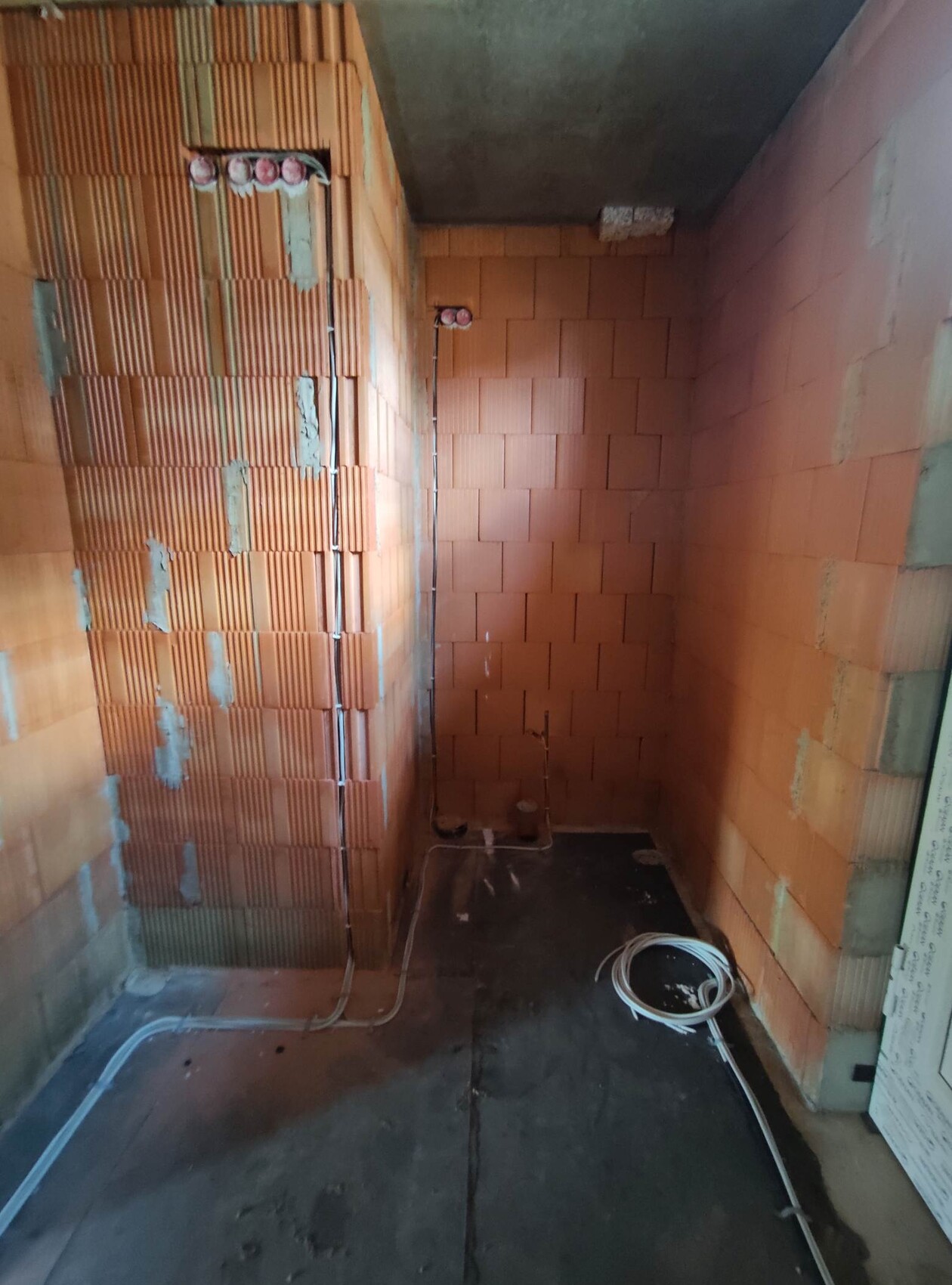 Tight construction area with red brick, visible electrical cables and wires on the floor.
