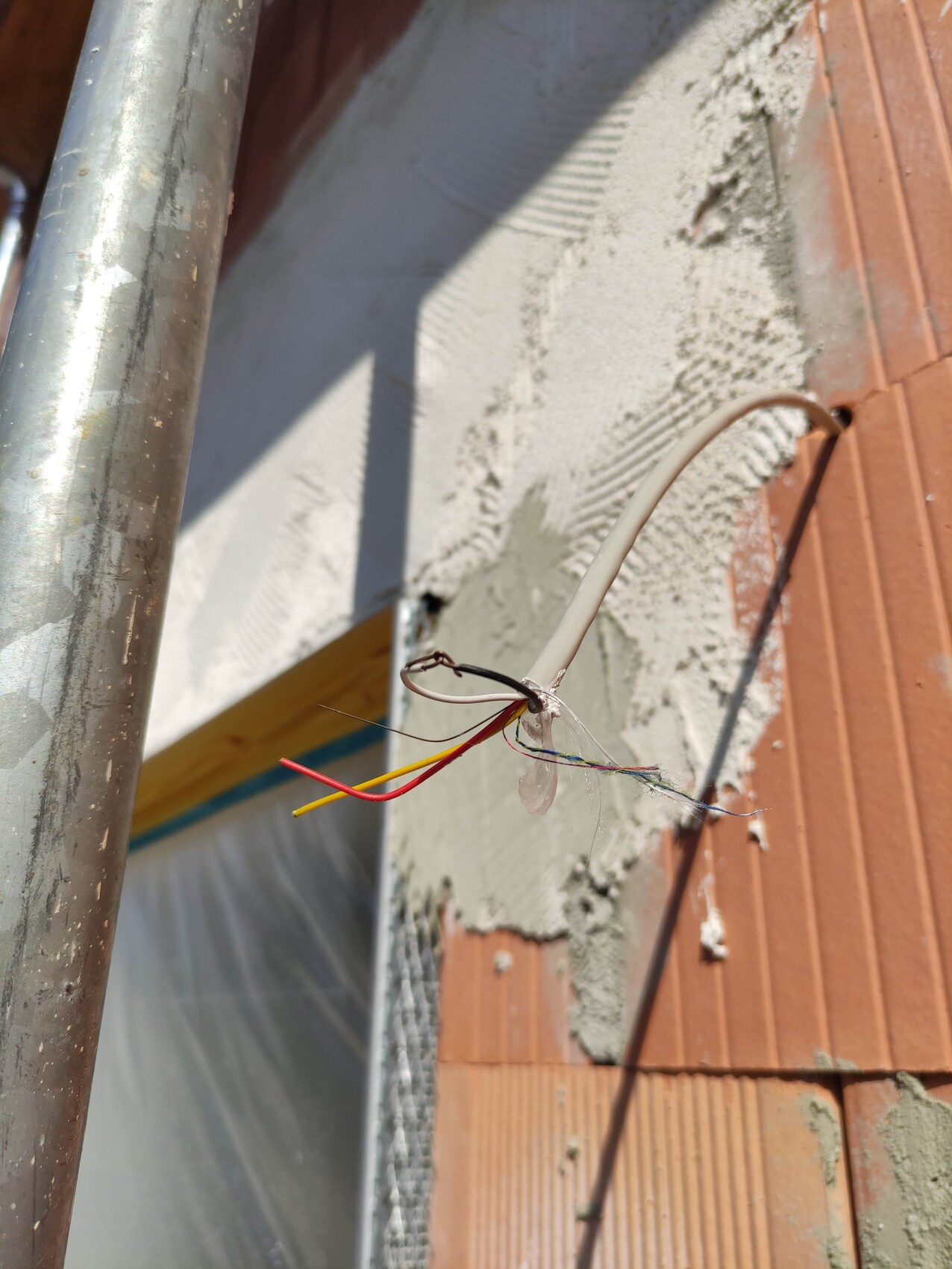 Exposed cable cores (red, yellow, blue) from exposed sheathing on a brick wall with plaster remnants