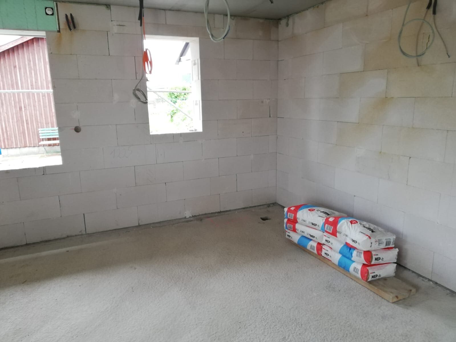 Unfinished interior with white blocks, hanging cables, window opening, and building material packages on the floor.