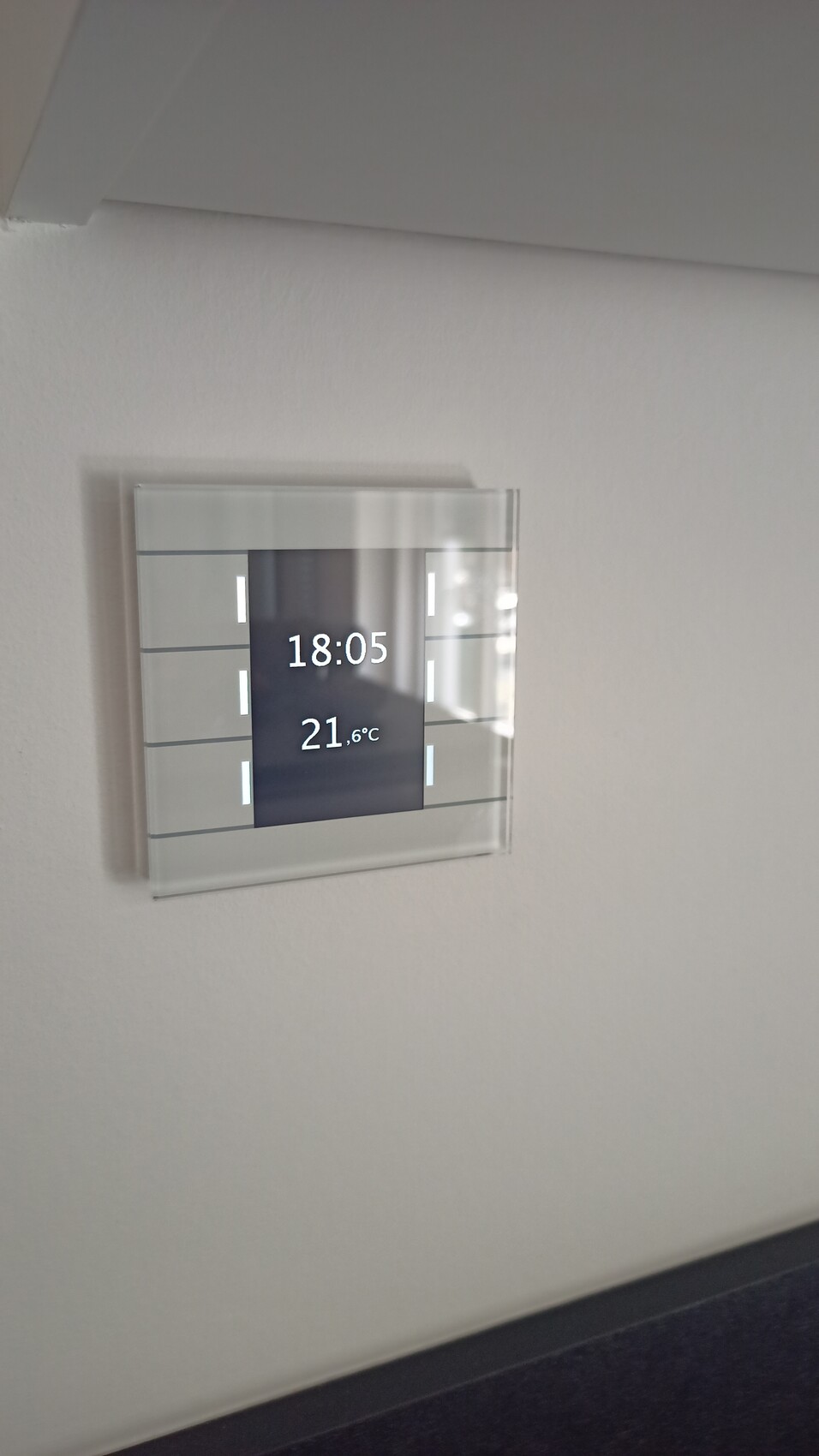 Digital wall display shows time 18:05 and temperature 21.6°C in a glass frame.