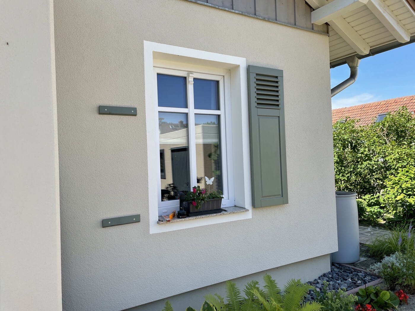 Außenansicht eines Hauses mit weißem Fensterrahmen, grünem Fensterladen und Blumenkasten.