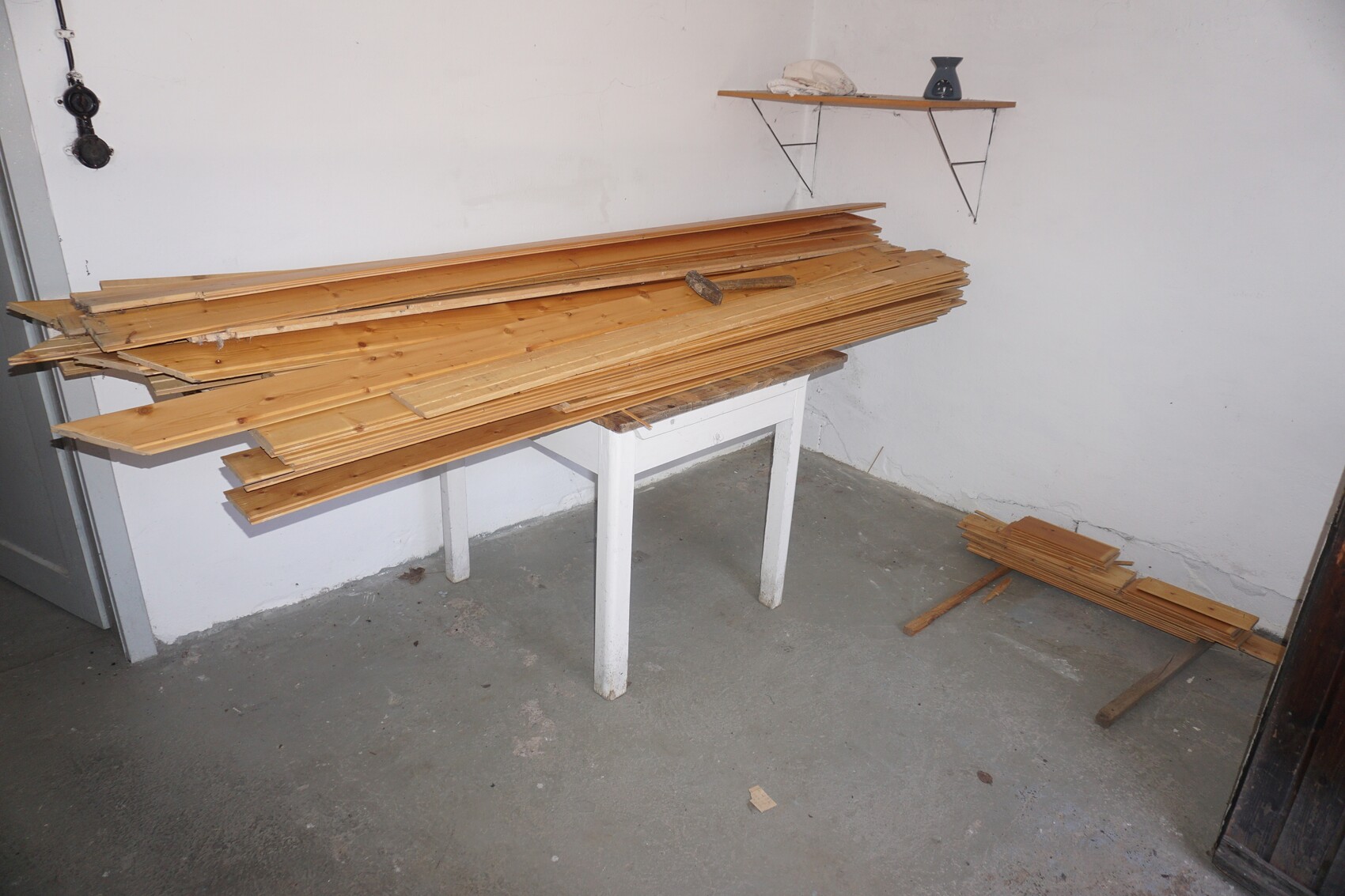 Many wooden slats stacked on a white workbench, more boards lying on the floor.