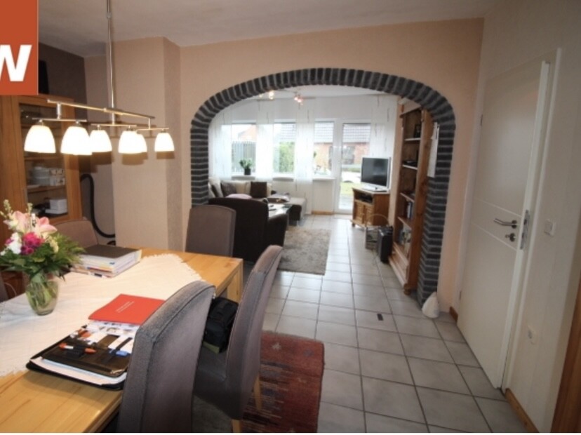 Open living and dining area through a stone arch; dining table, chairs, flowers, and TV.