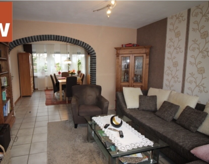 Living room with gray sofa, armchair, and glass table; view of dining area through stone arch.