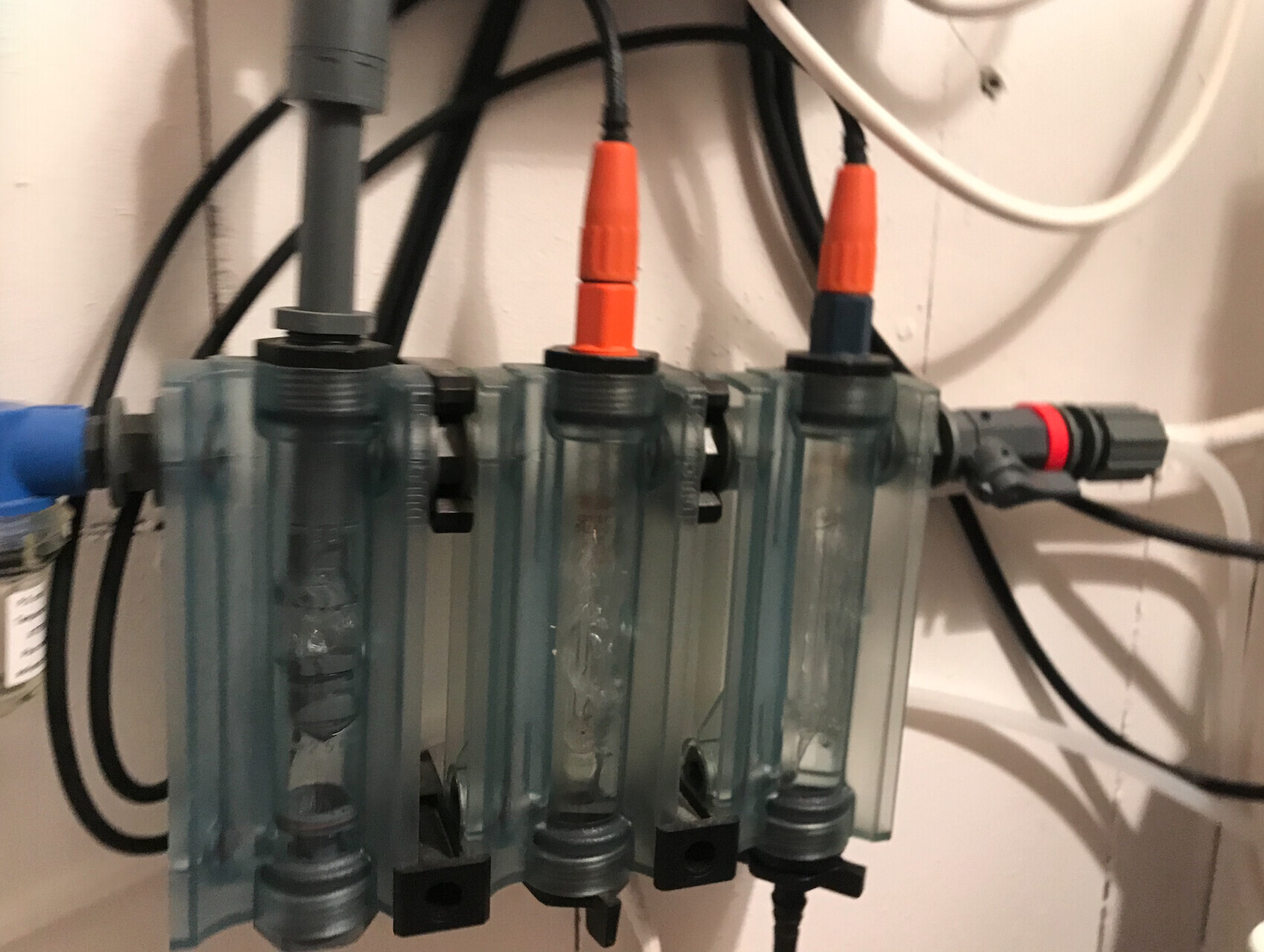 Vier graue Kunststoff-Verteilerblöcke mit transparenten Röhren und orange/blau Kupplungen.