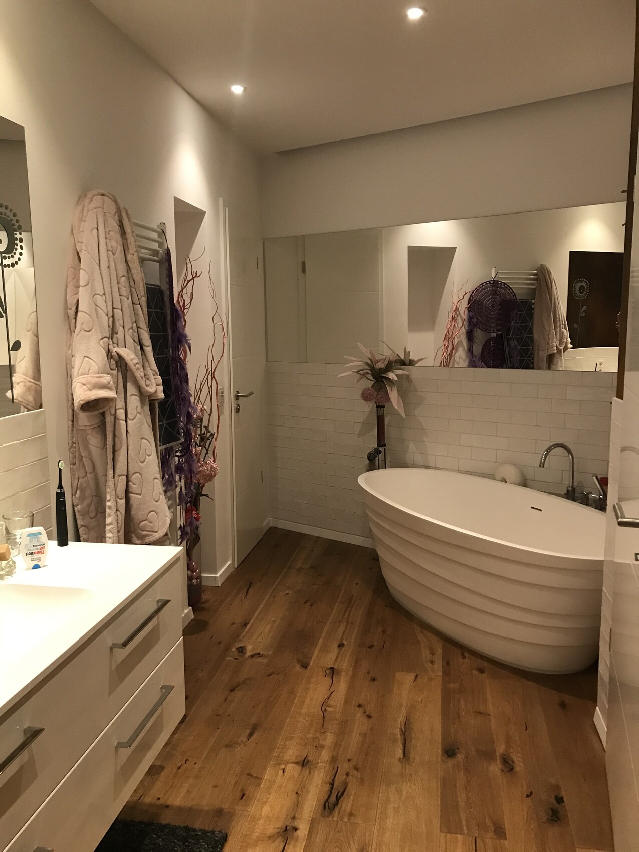 Modern bathroom with freestanding bathtub, wooden floor, and mirror.