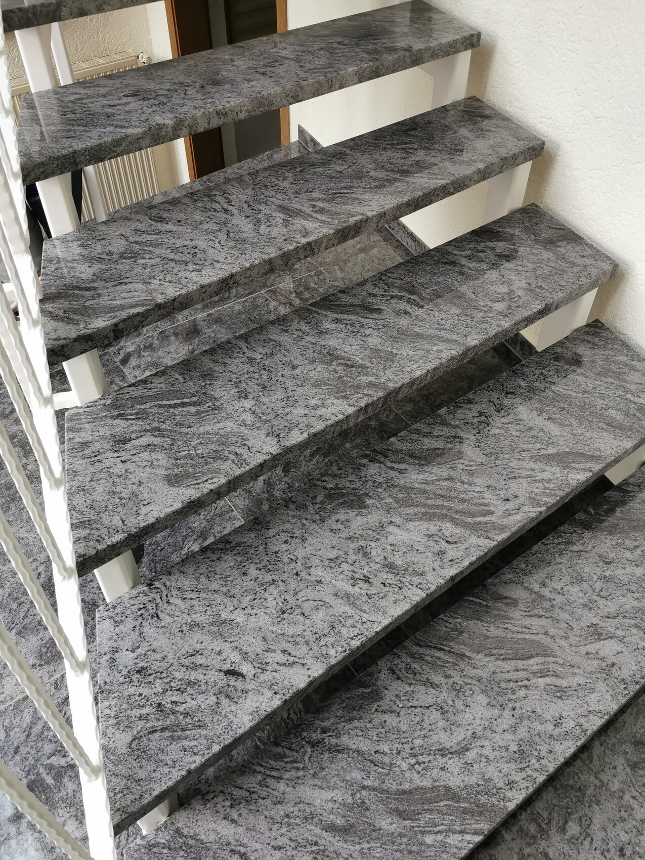 Modern staircase made of grey granite with open steps against a white wall