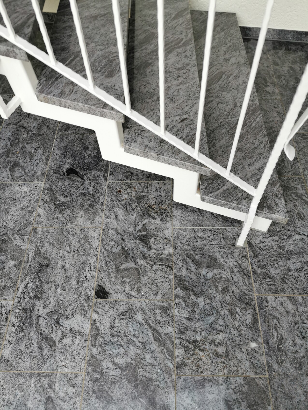 Top view of a grey stone step staircase with white railing indoors.