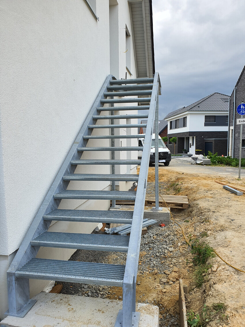 Exterior steel staircase attached to a white house; construction area and residential neighborhood in the background.