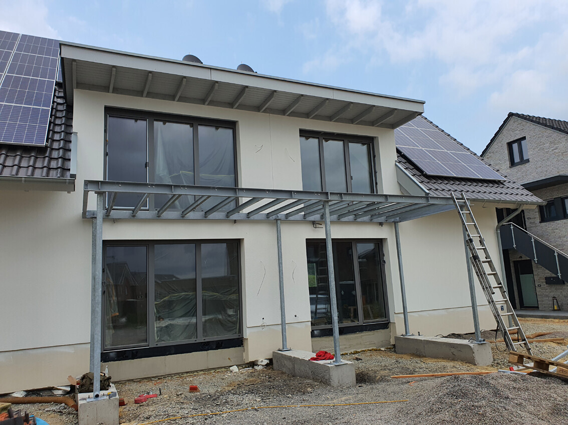 Two-story house under construction with metal scaffolding, ladder, and solar panels on the roof.