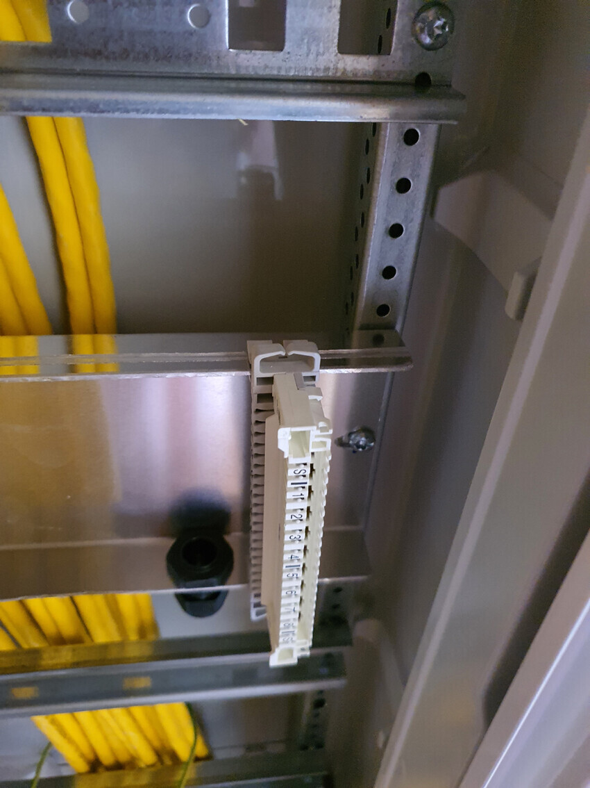 Control cabinet: white terminal block on DIN rail, yellow cables beside it.