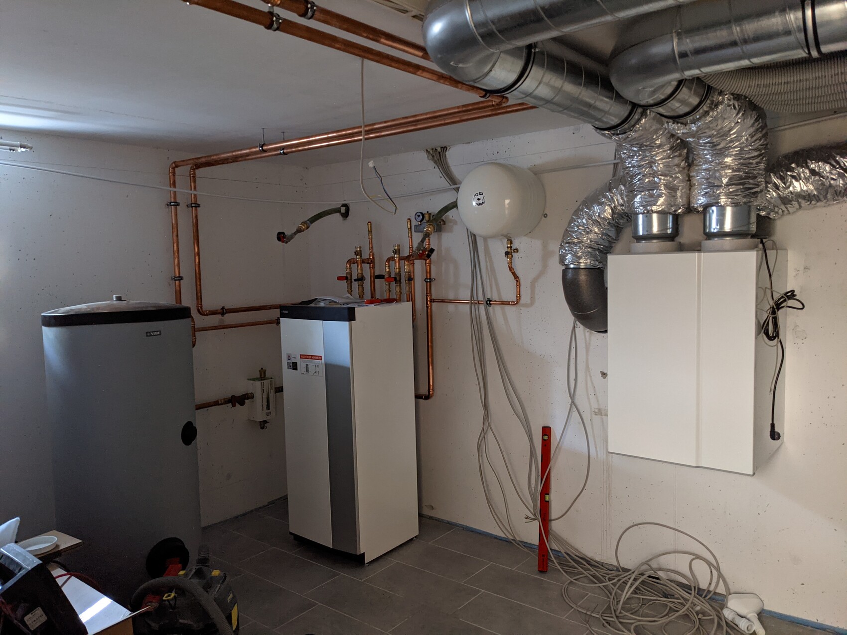 Basement room with heating system: copper pipes, hot water tank, boiler, and ventilation ducts.