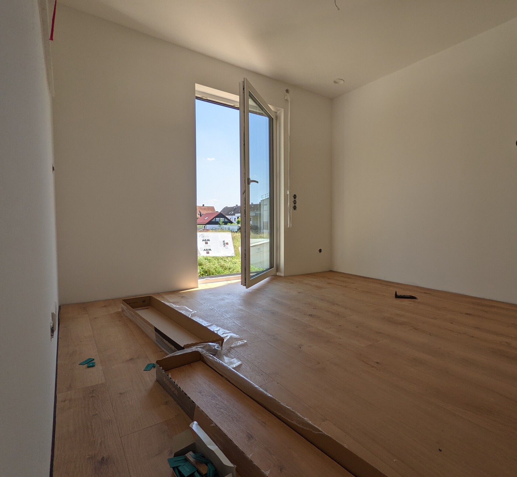 Empty living space with open glass door to the balcony, wooden floor, building materials on the floor.