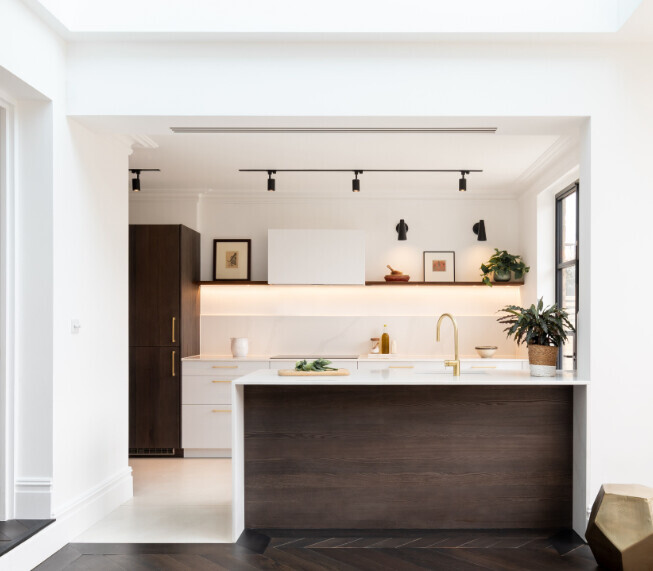 Modern kitchen with island, white cabinets, dark base units, and gold faucet in a bright room