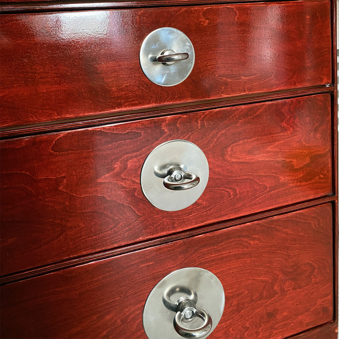 Red wooden chest of drawers with three drawers and round metal handles.