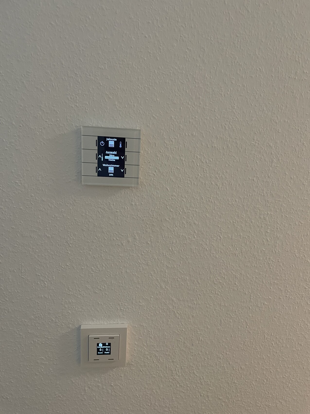 White wall with two digital control units: large screen on top, smaller panel below.