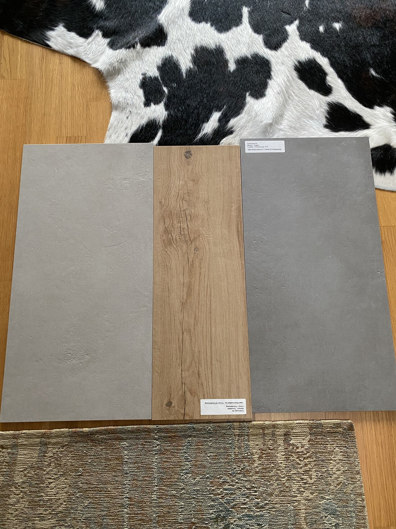 Three floor covering samples: gray concrete-look and brown wood-look tiles placed side by side on wooden floor