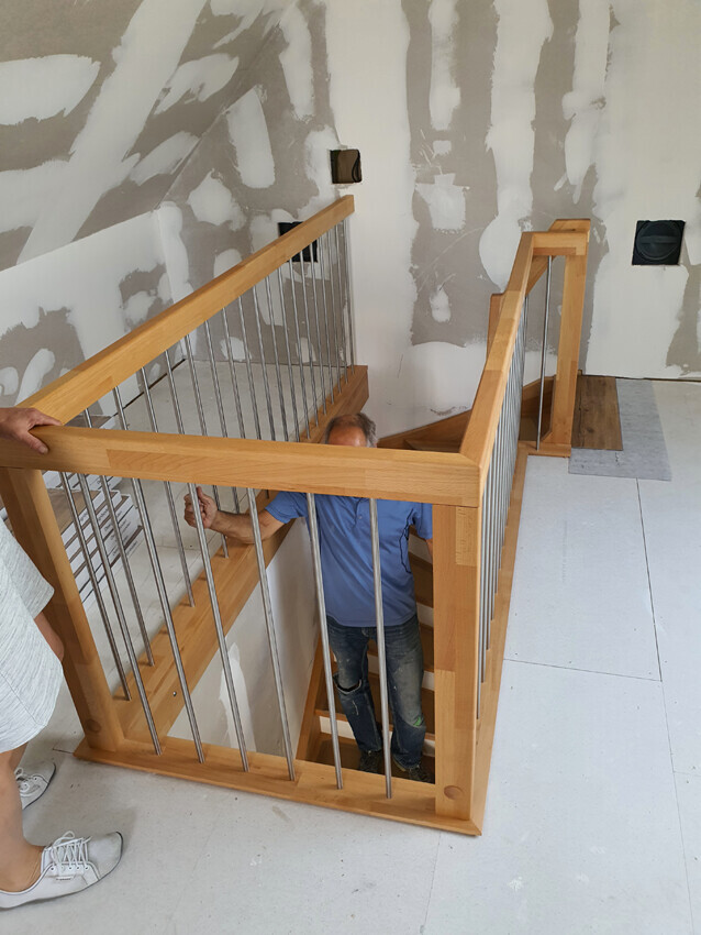 Staircase with wooden handrail and metal rods in shell construction; two people at the handrail.