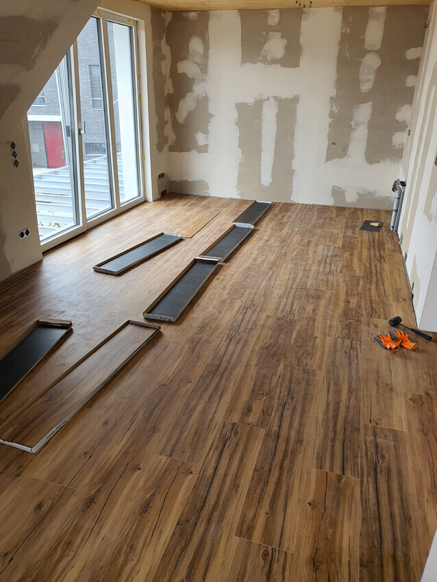 Renovation room with wooden floor; floor panels laid, unfinished walls, window front.