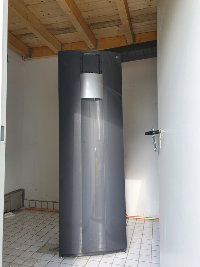 Large dark boiler in basement room with wooden beam ceiling and door handle on the right
