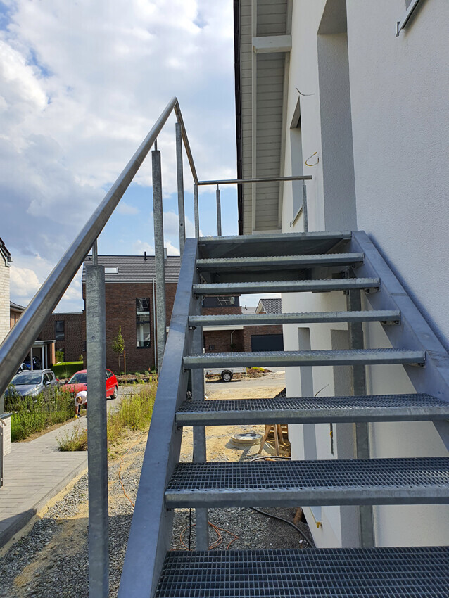 Exterior metal staircase on white building facade, steps leading up, construction site surroundings in the background.