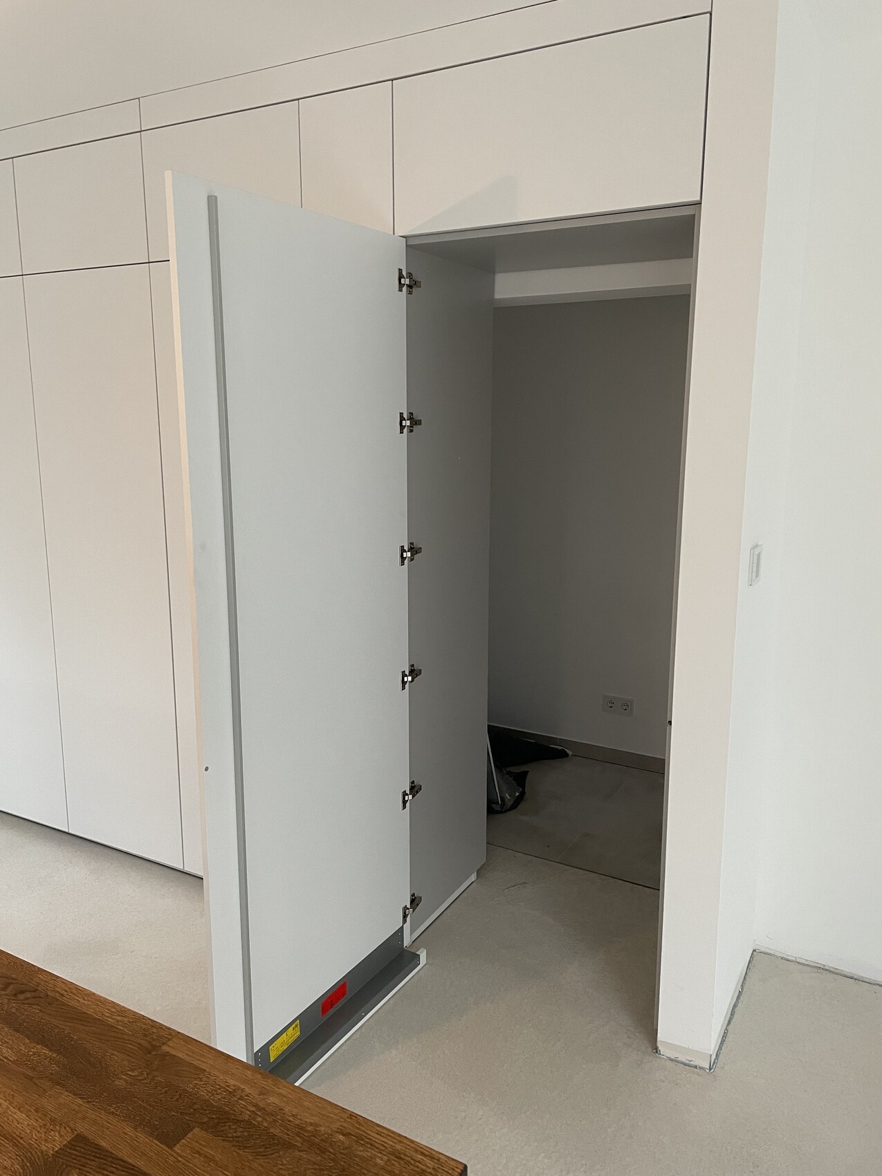 Open white built-in cabinet door in a modern interior, grey inside, wooden table in the foreground.