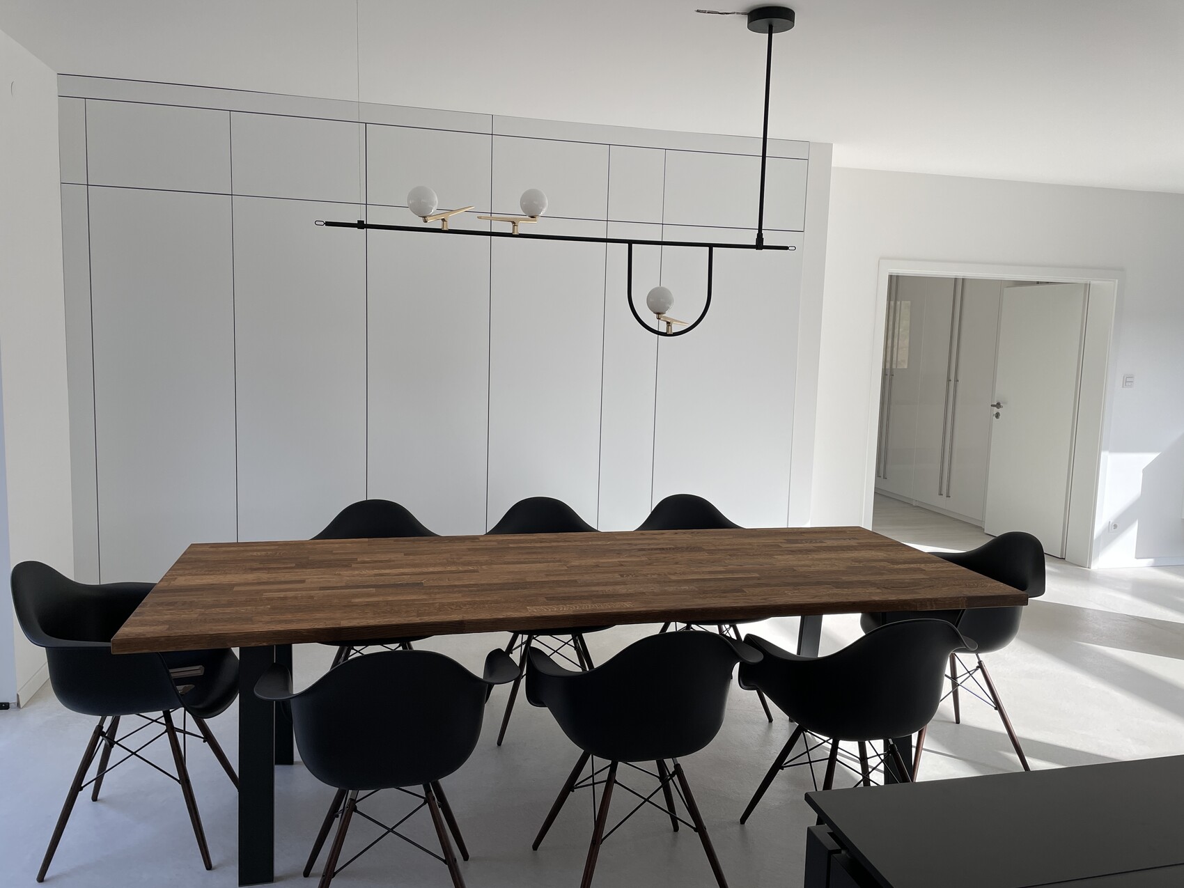 Modern dining room with long wooden table, black chairs, and white cabinets.