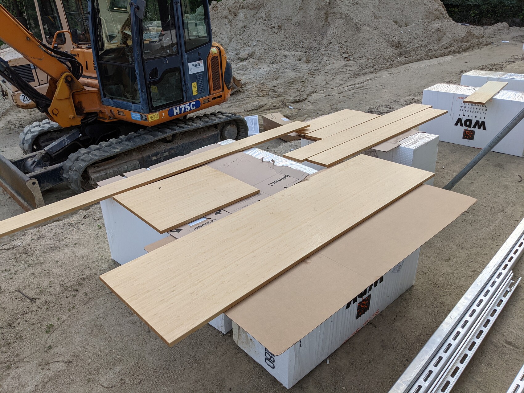 Small excavator on construction site; wooden boards lying on white Styrofoam boxes next to metal rods.