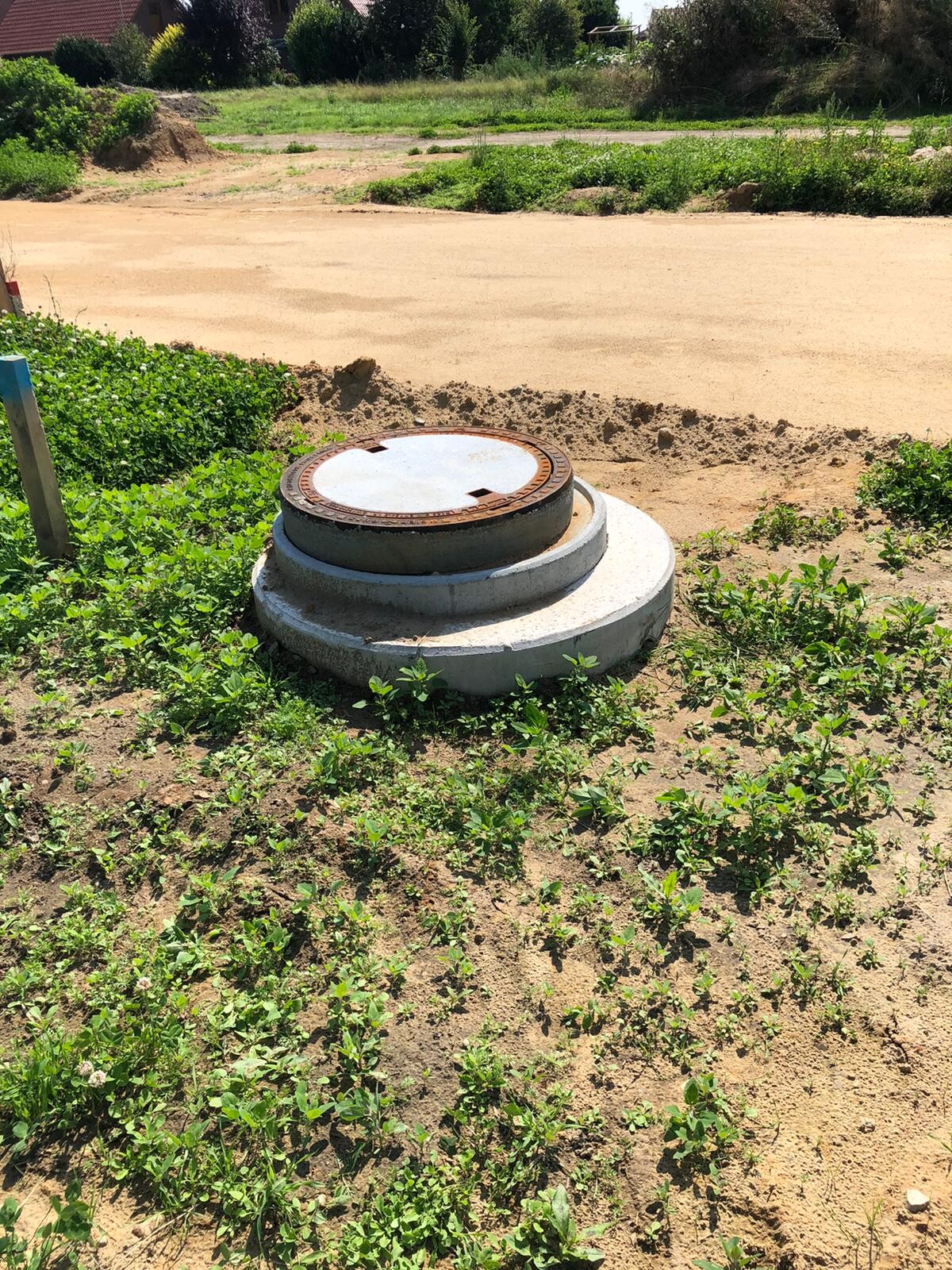 Rusted metal cover on a gray concrete slab in sandy terrain, surrounded by grass.