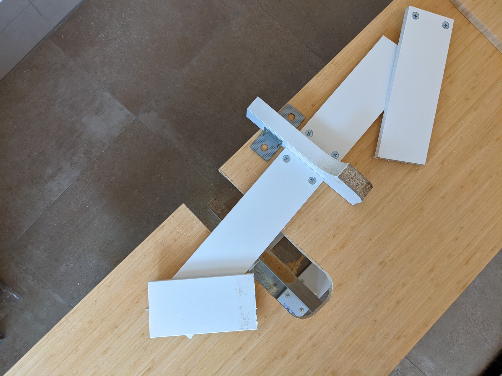 White metal parts and brackets on wooden table, assembly kit with screws.