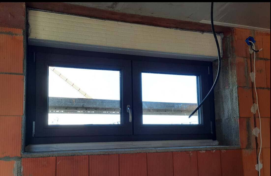 Double-glazed window in shell construction with blue frame, red brick wall and cables.