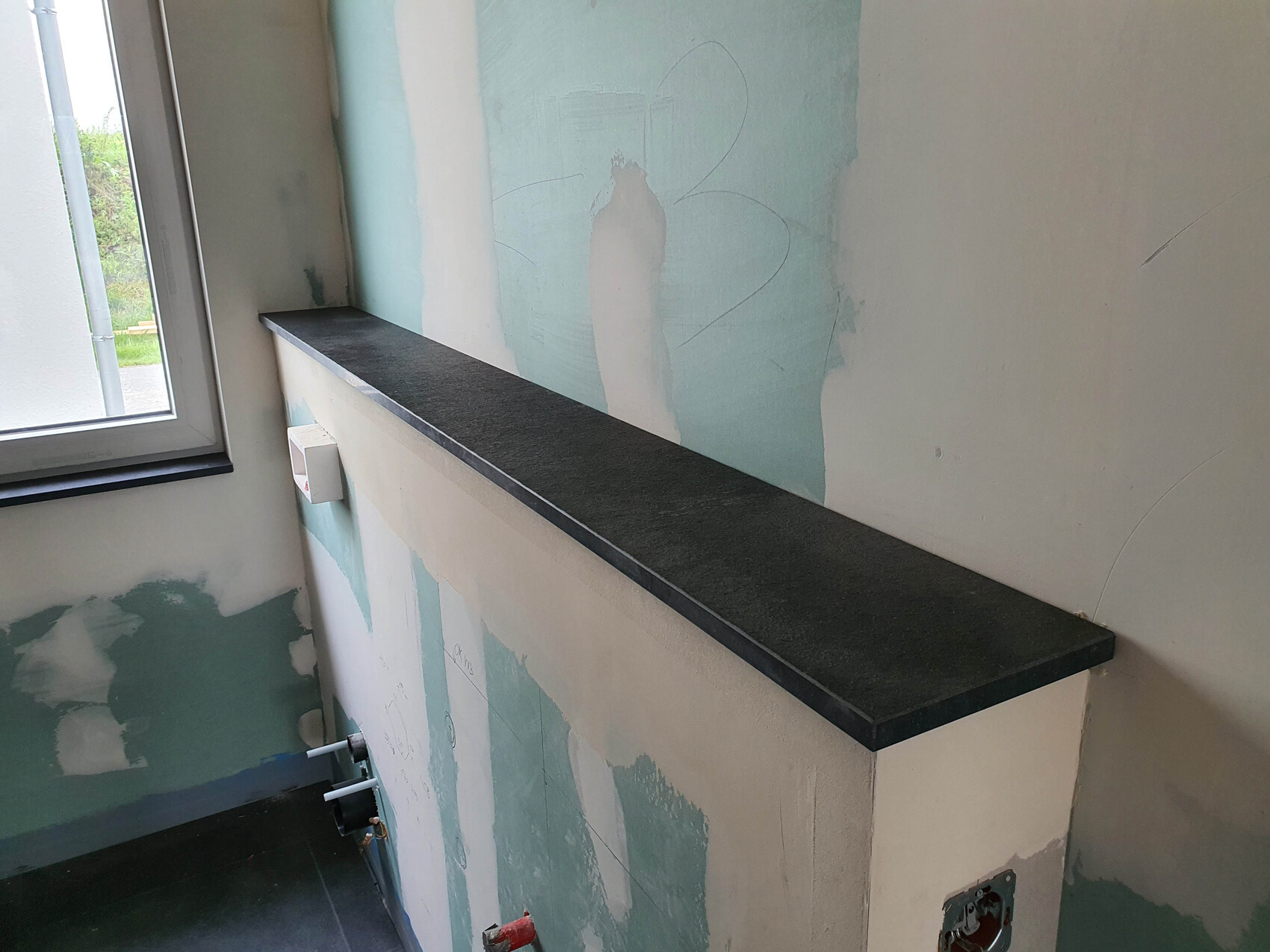 Long dark stone slab as a work surface on a half-finished wall next to the window.